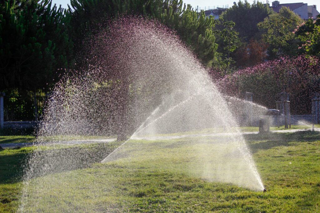 Water sprinkler system spraying lush green grass in a sunny outdoor setting, ideal for lawn care illustrations.