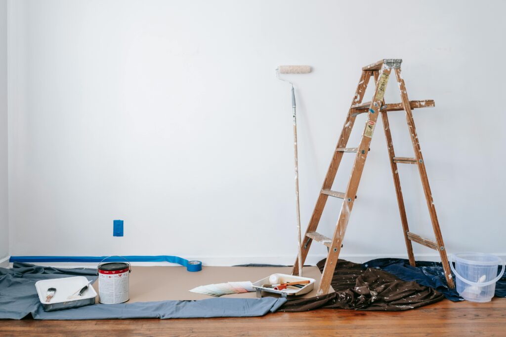 A room prepared for renovation with a ladder, paint supplies, and drop cloth.