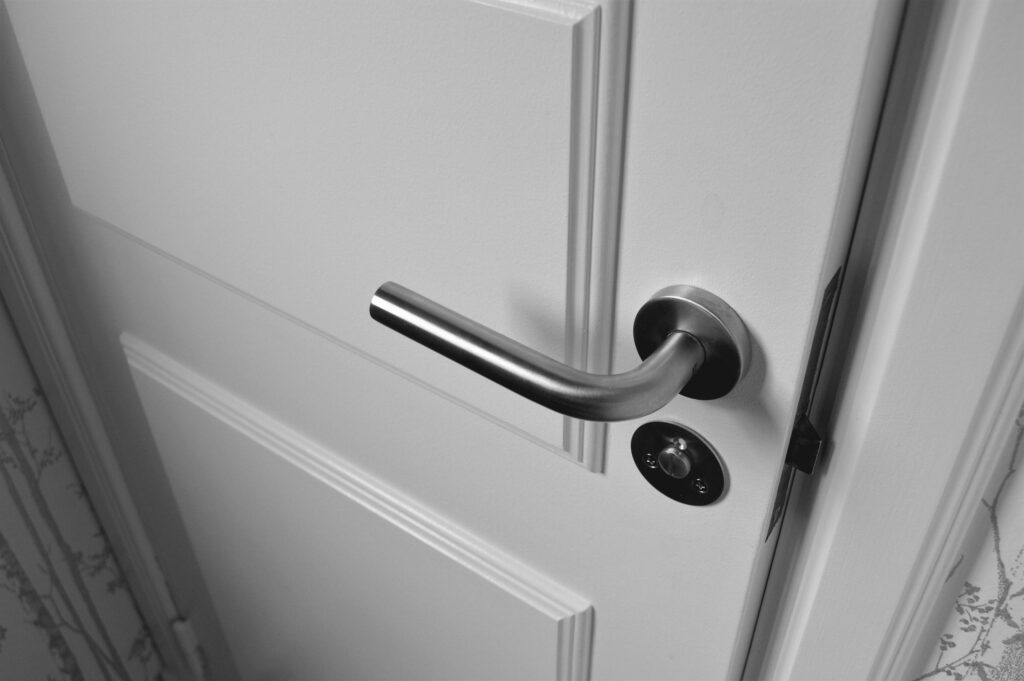 Close-up of a sleek steel door handle on a white door, showcasing modern interior design in monochrome.