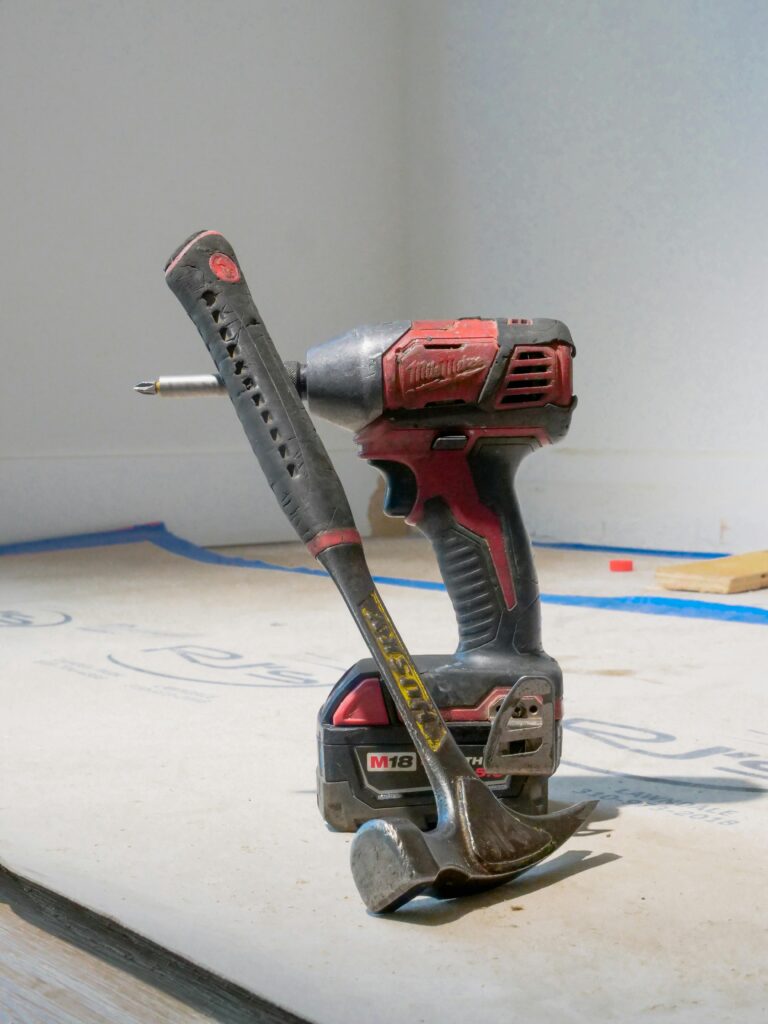 Close-up of a power drill and hammer on a construction site floor.